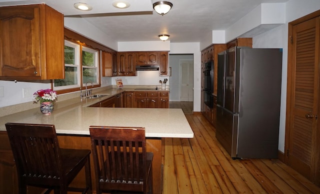 kitchen with kitchen peninsula, a breakfast bar, black appliances, and light hardwood / wood-style flooring