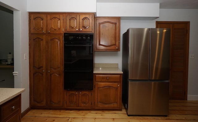 kitchen with light hardwood / wood-style floors, black double oven, and stainless steel refrigerator