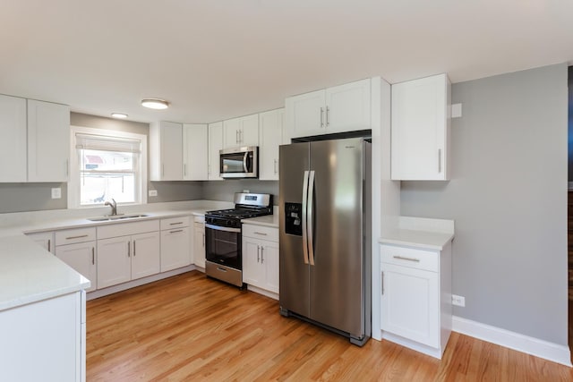 kitchen with a sink, light wood-type flooring, light countertops, white cabinets, and appliances with stainless steel finishes