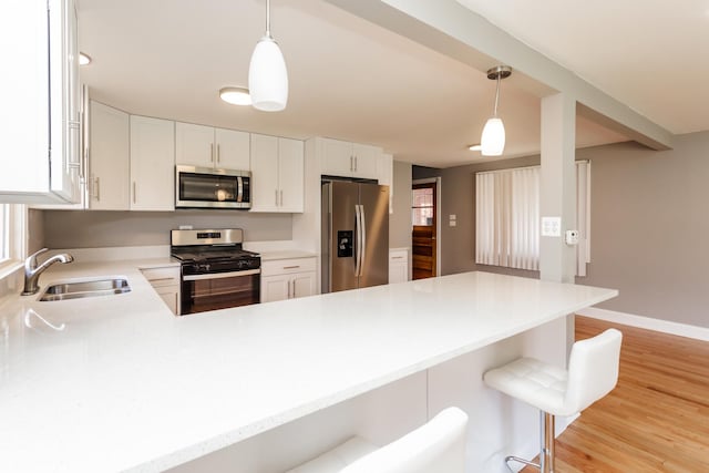 kitchen featuring stainless steel appliances, light countertops, a kitchen bar, a peninsula, and decorative light fixtures