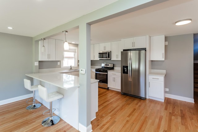 kitchen with a sink, light wood-style floors, a kitchen bar, light countertops, and appliances with stainless steel finishes
