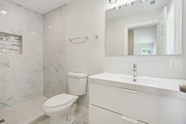 bathroom featuring a tile shower, vanity, and toilet