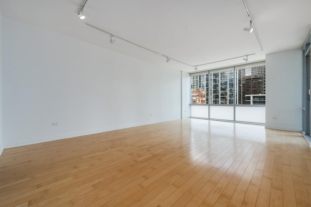 empty room featuring rail lighting, light hardwood / wood-style floors, and expansive windows