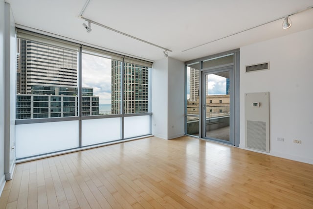 empty room featuring expansive windows, light hardwood / wood-style floors, and track lighting