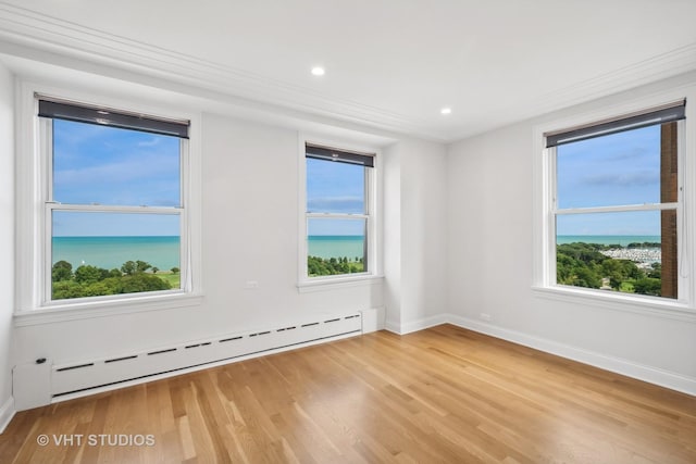 empty room featuring a baseboard heating unit, a water view, and hardwood / wood-style floors