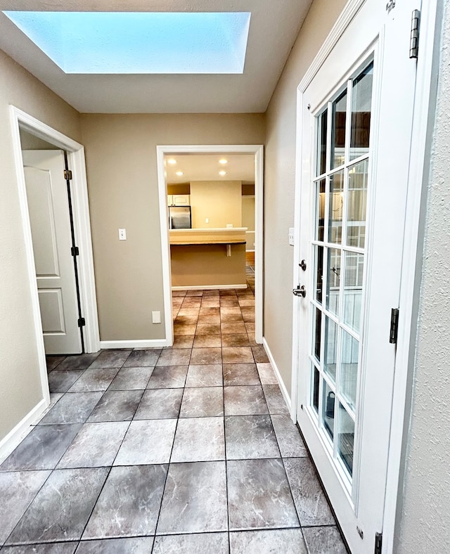 hall with a skylight, baseboards, and dark tile patterned flooring