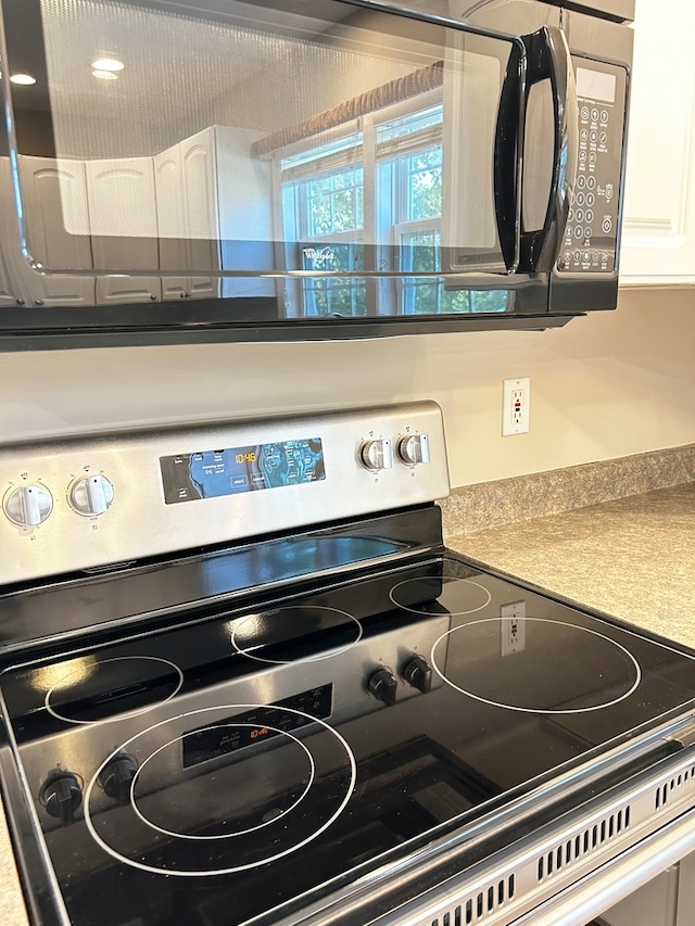 interior details featuring black microwave, light countertops, stainless steel range with electric stovetop, and white cabinets