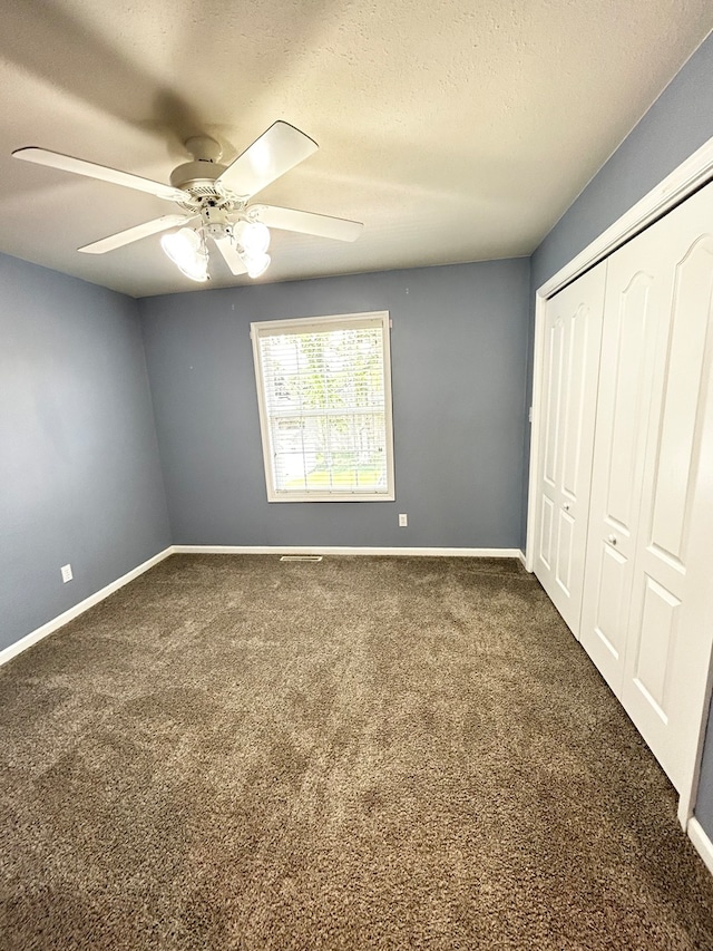 unfurnished bedroom with a textured ceiling, a ceiling fan, baseboards, a closet, and dark colored carpet