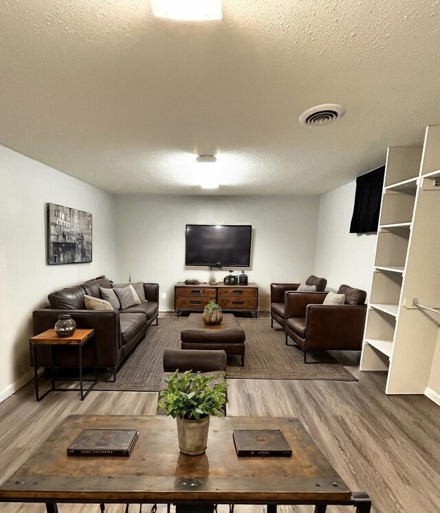 living area with baseboards, a textured ceiling, visible vents, and wood finished floors