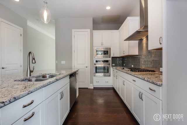 kitchen featuring wall chimney exhaust hood, stainless steel appliances, sink, white cabinets, and hanging light fixtures