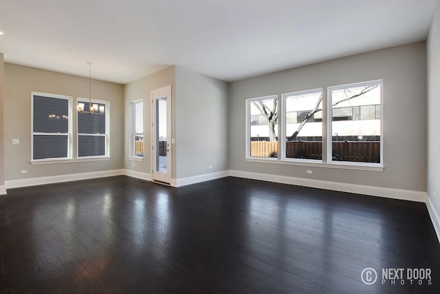 unfurnished living room with dark hardwood / wood-style floors, a wealth of natural light, and an inviting chandelier