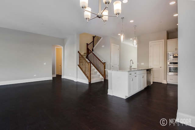 kitchen featuring appliances with stainless steel finishes, light stone counters, a center island with sink, white cabinets, and hanging light fixtures