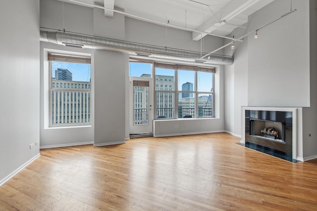 unfurnished living room with a towering ceiling, a fireplace with flush hearth, wood finished floors, a view of city, and track lighting