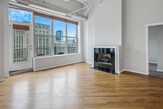 unfurnished living room with a fireplace with flush hearth, a towering ceiling, wood finished floors, and visible vents