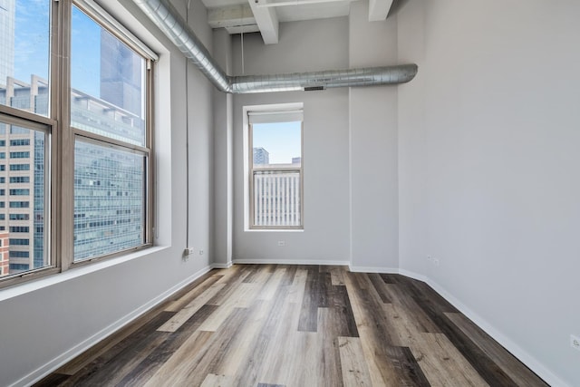 unfurnished room featuring beam ceiling, baseboards, and wood finished floors