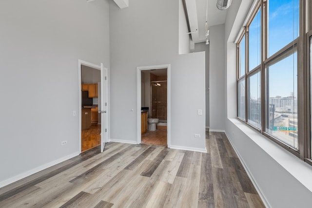 unfurnished bedroom with baseboards, visible vents, ensuite bath, wood finished floors, and a high ceiling