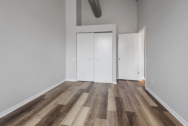 unfurnished bedroom with a high ceiling, a closet, wood finished floors, and baseboards