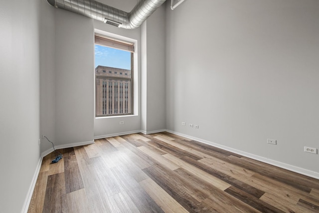 spare room featuring wood finished floors, visible vents, and baseboards