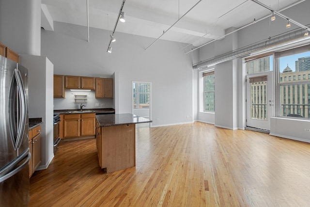 kitchen with a center island, brown cabinets, light wood-style flooring, a high ceiling, and freestanding refrigerator