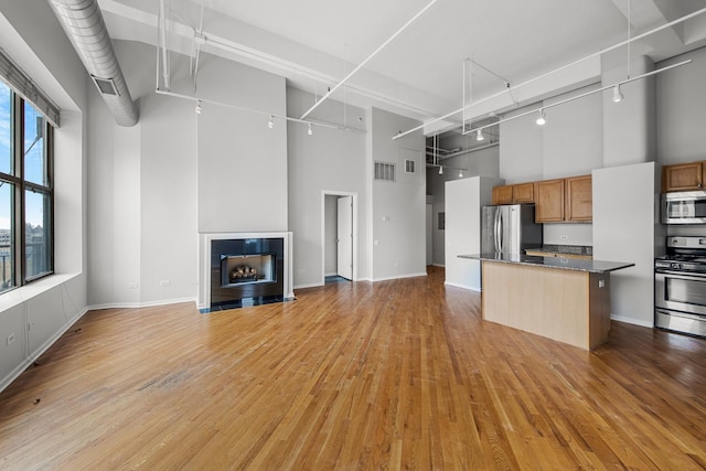 kitchen featuring appliances with stainless steel finishes, light wood-style flooring, a tile fireplace, and a high ceiling