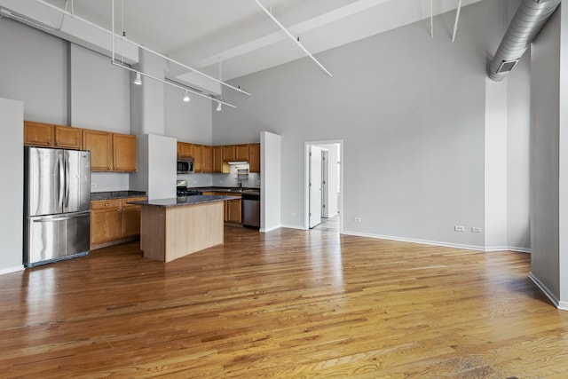 kitchen featuring stainless steel appliances, dark countertops, a towering ceiling, open floor plan, and wood finished floors