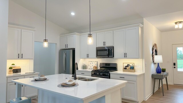 kitchen with appliances with stainless steel finishes, white cabinets, vaulted ceiling, backsplash, and a kitchen island with sink