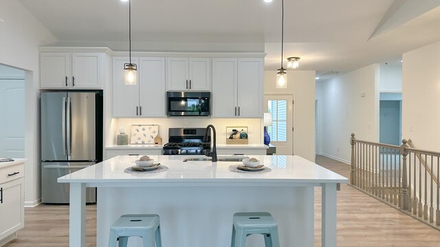 kitchen with appliances with stainless steel finishes, white cabinetry, light wood-type flooring, and a kitchen island with sink