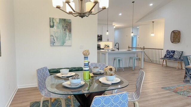 dining space with a notable chandelier, vaulted ceiling, sink, and light wood-type flooring