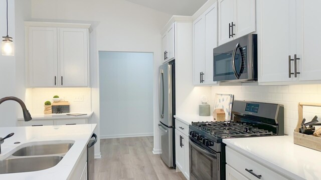 kitchen with white cabinetry, stainless steel appliances, hanging light fixtures, sink, and light hardwood / wood-style floors