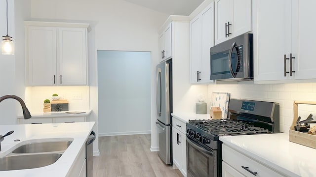 kitchen featuring appliances with stainless steel finishes, decorative light fixtures, light countertops, white cabinetry, and a sink