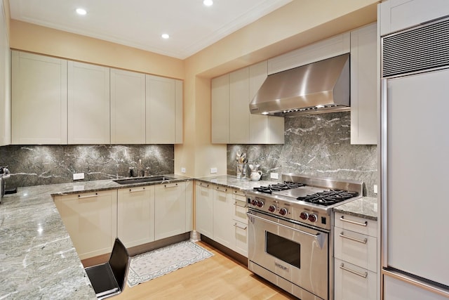 kitchen with white cabinetry, light stone counters, high quality appliances, and wall chimney range hood