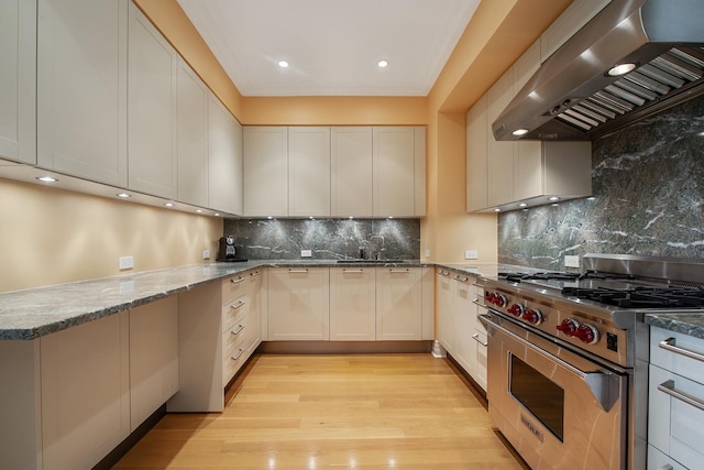 kitchen featuring white cabinets, luxury range, wall chimney exhaust hood, tasteful backsplash, and light stone counters