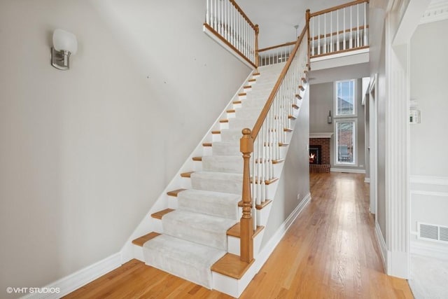 stairs featuring a fireplace, wood-type flooring, and a high ceiling