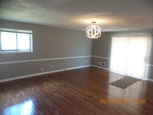 empty room featuring a textured ceiling, an inviting chandelier, and dark wood-type flooring