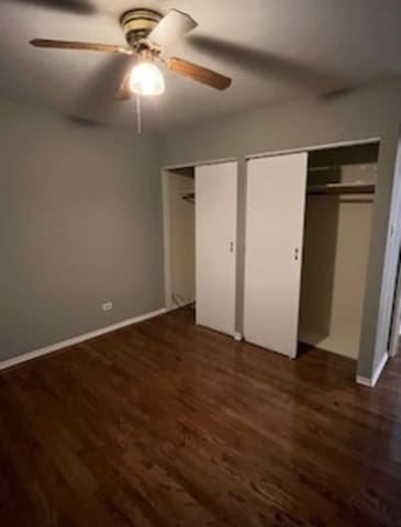 unfurnished bedroom with multiple closets, ceiling fan, and dark wood-type flooring