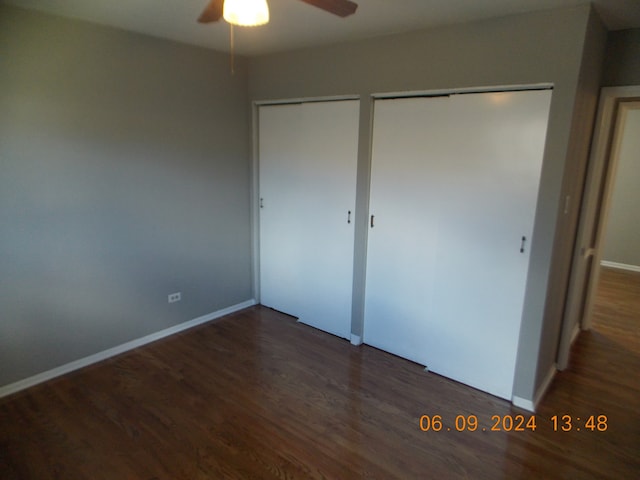 unfurnished bedroom with two closets, ceiling fan, and dark wood-type flooring