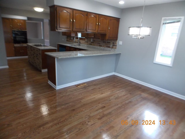 kitchen with kitchen peninsula, dark hardwood / wood-style flooring, black appliances, sink, and hanging light fixtures