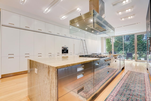 kitchen featuring white cabinetry, a wall of windows, a spacious island, and light stone counters