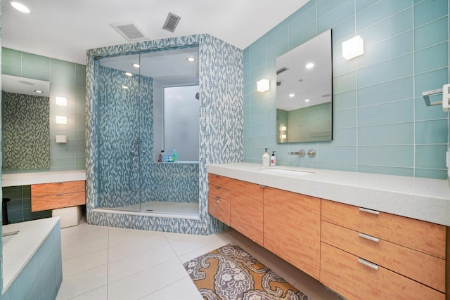 bathroom with tile patterned flooring, vanity, a tile shower, and tile walls