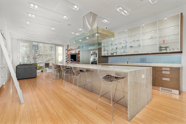 kitchen with a breakfast bar, backsplash, a spacious island, light wood-type flooring, and light stone countertops