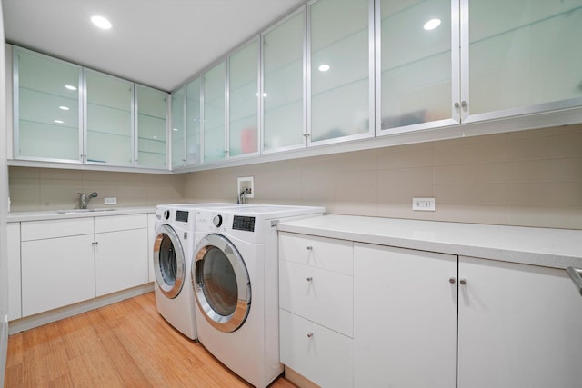 washroom with light hardwood / wood-style flooring, cabinets, sink, and washing machine and clothes dryer