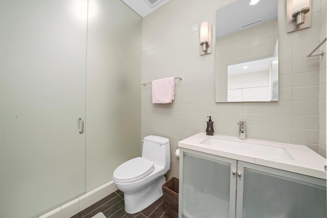 bathroom with vanity, a shower with shower door, tile walls, and toilet