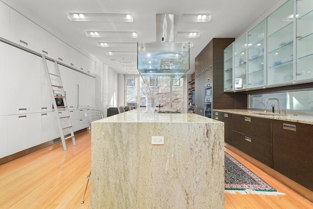 kitchen featuring light stone counters, a center island with sink, light hardwood / wood-style floors, and sink