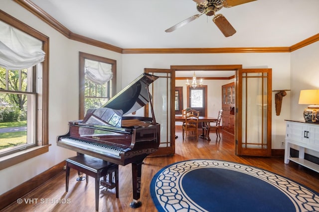 living area with baseboards, wood finished floors, ornamental molding, and ceiling fan with notable chandelier