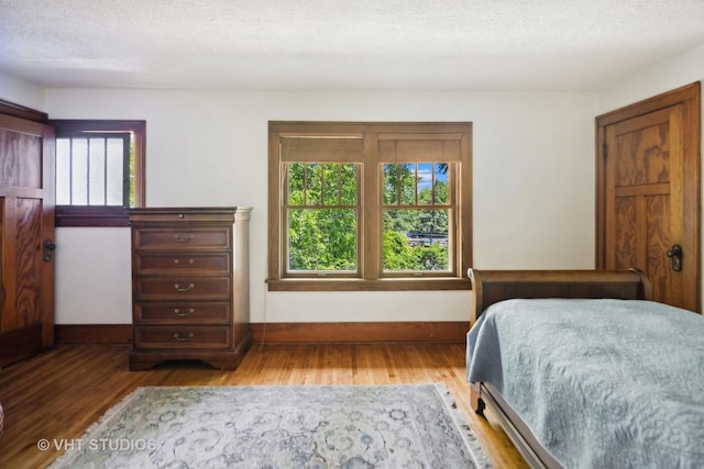 bedroom with wood finished floors, baseboards, and a textured ceiling