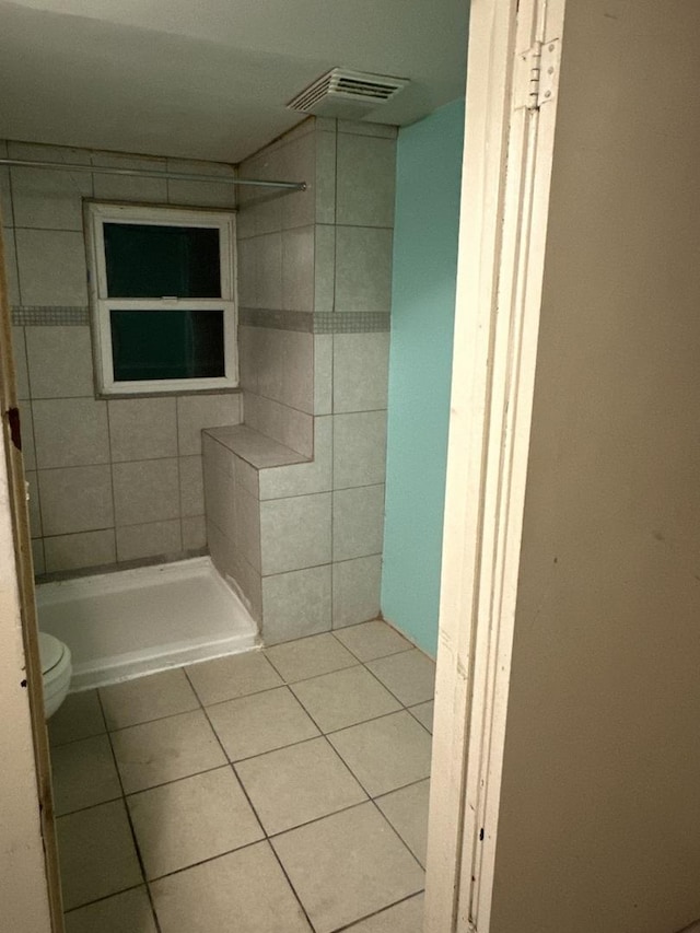 bathroom with tile patterned flooring, toilet, and tiled shower