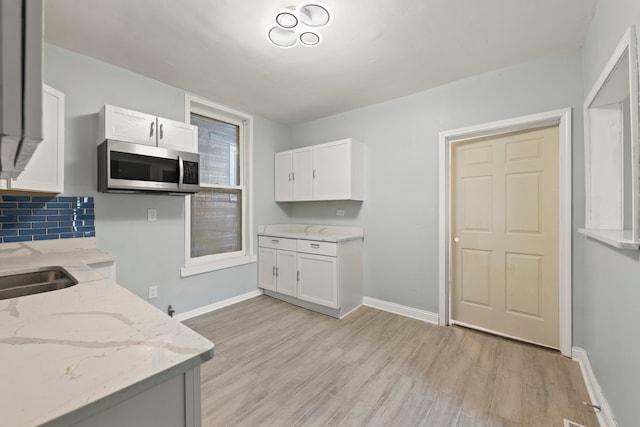 kitchen with light stone countertops, tasteful backsplash, white cabinets, and light wood-type flooring