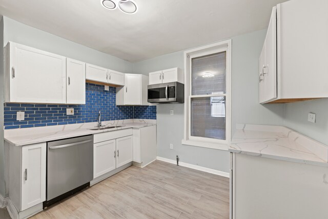 kitchen featuring light stone countertops, stainless steel appliances, light wood-type flooring, sink, and white cabinets