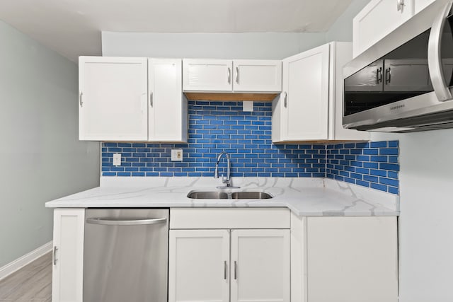 kitchen with light hardwood / wood-style floors, stainless steel appliances, light stone countertops, white cabinets, and sink