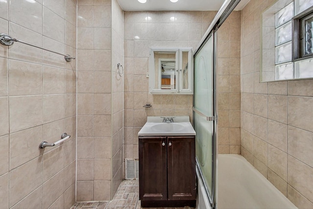 bathroom featuring vanity, tile walls, and combined bath / shower with glass door